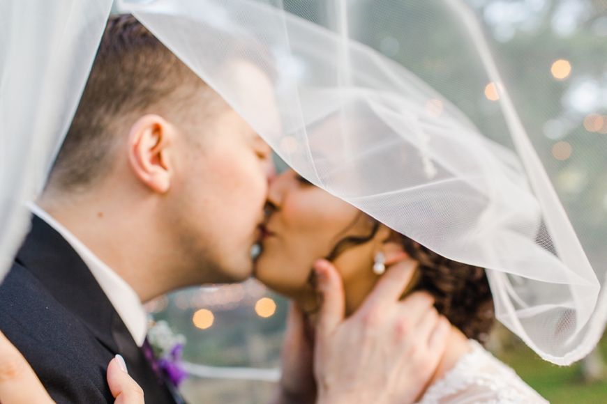 A tender wedding kiss captured under a flowing white veil.