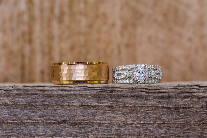 Two wedding rings, one gold and one diamond-encrusted, displayed on weathered wood.