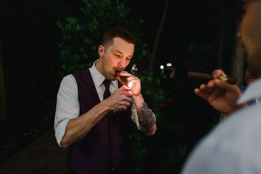A guest in purple vest lighting up a cigarette during nighttime wedding festivities.