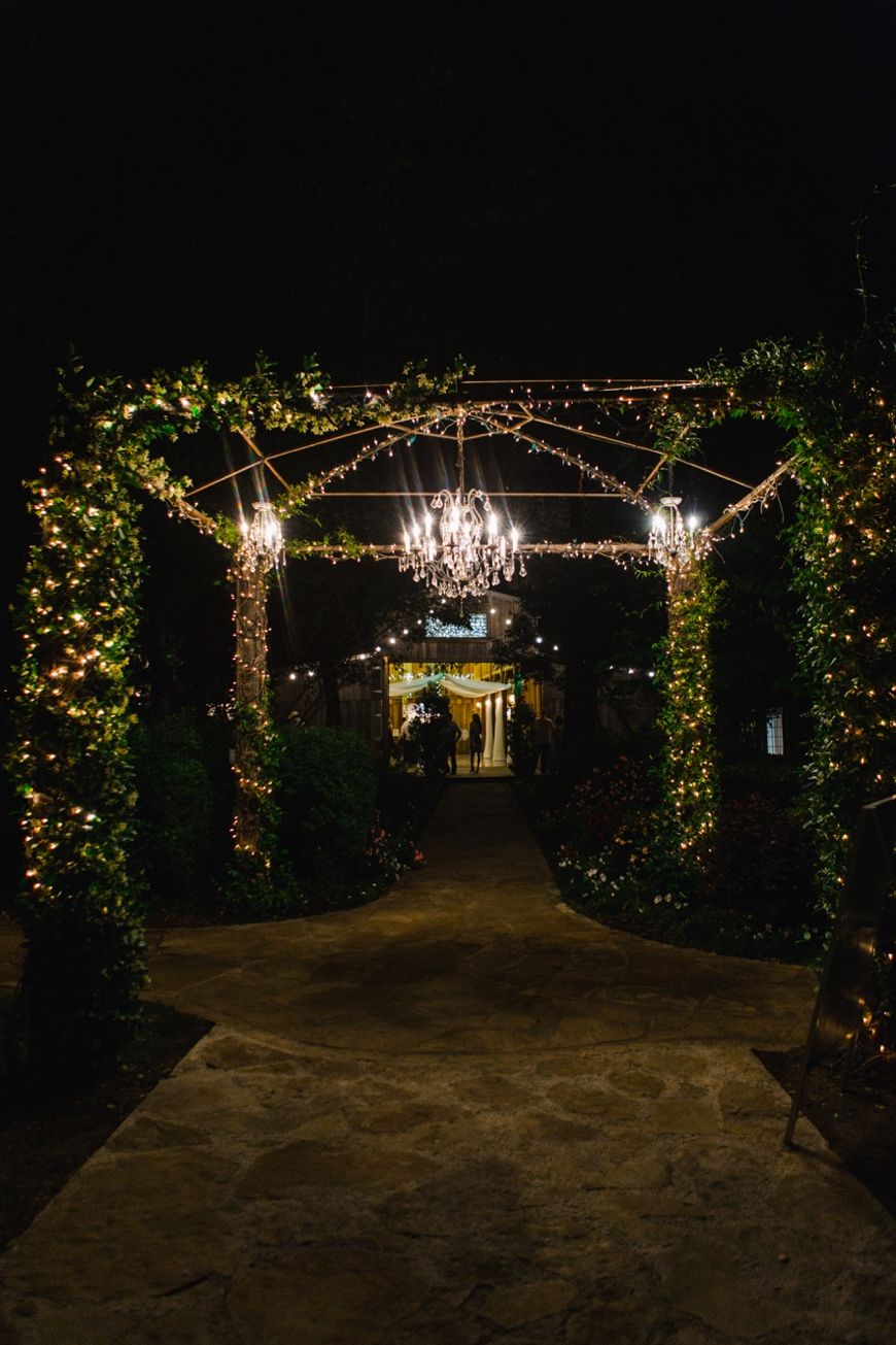 An illuminated wedding venue walkway with twinkling lights and chandeliers at night.