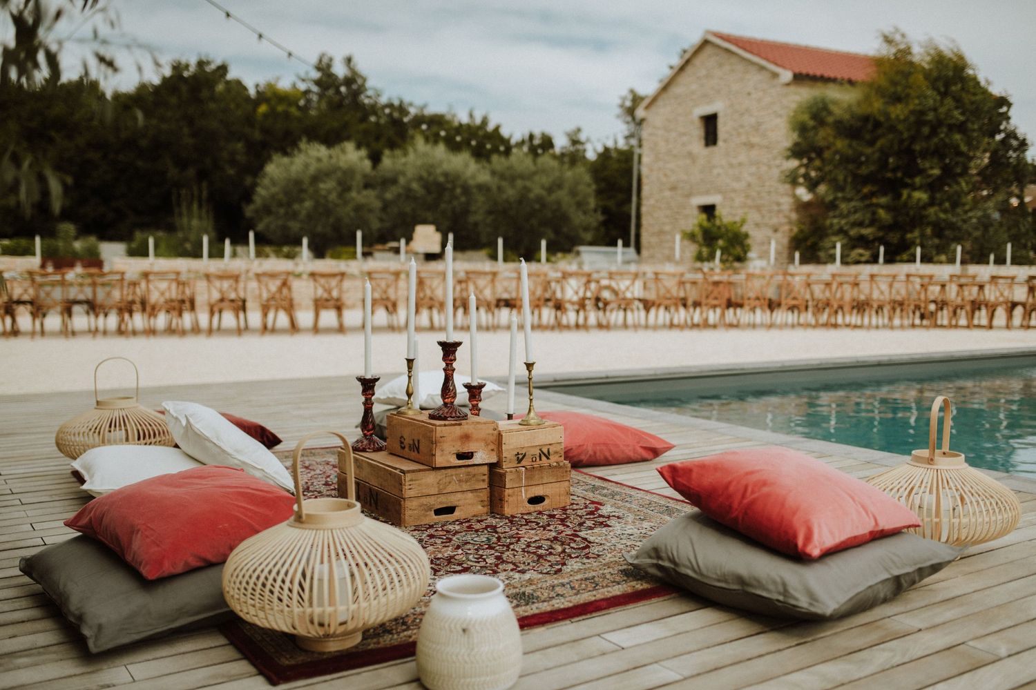 Cozy poolside picnic setup with floor cushions, wicker baskets and boho decor near a swimming pool at sunset.