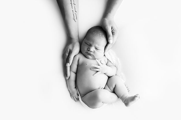 Black and white image of newborn baby girl on white blanket being held by dad.