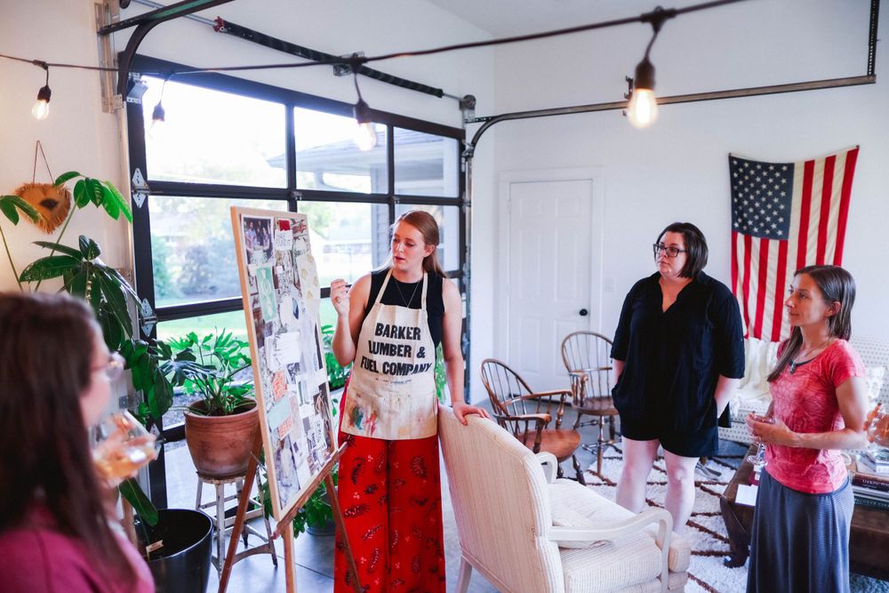 Participants gather around tables in a bright studio space for an art workshop with an American flag on display.