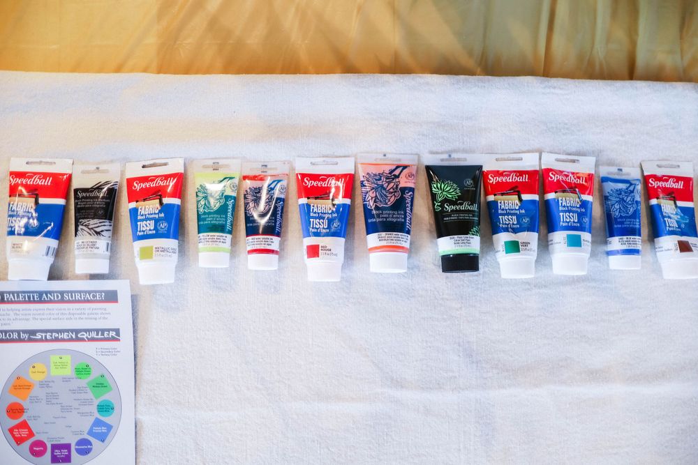 Row of colorful art supplies and materials arranged on a white surface.