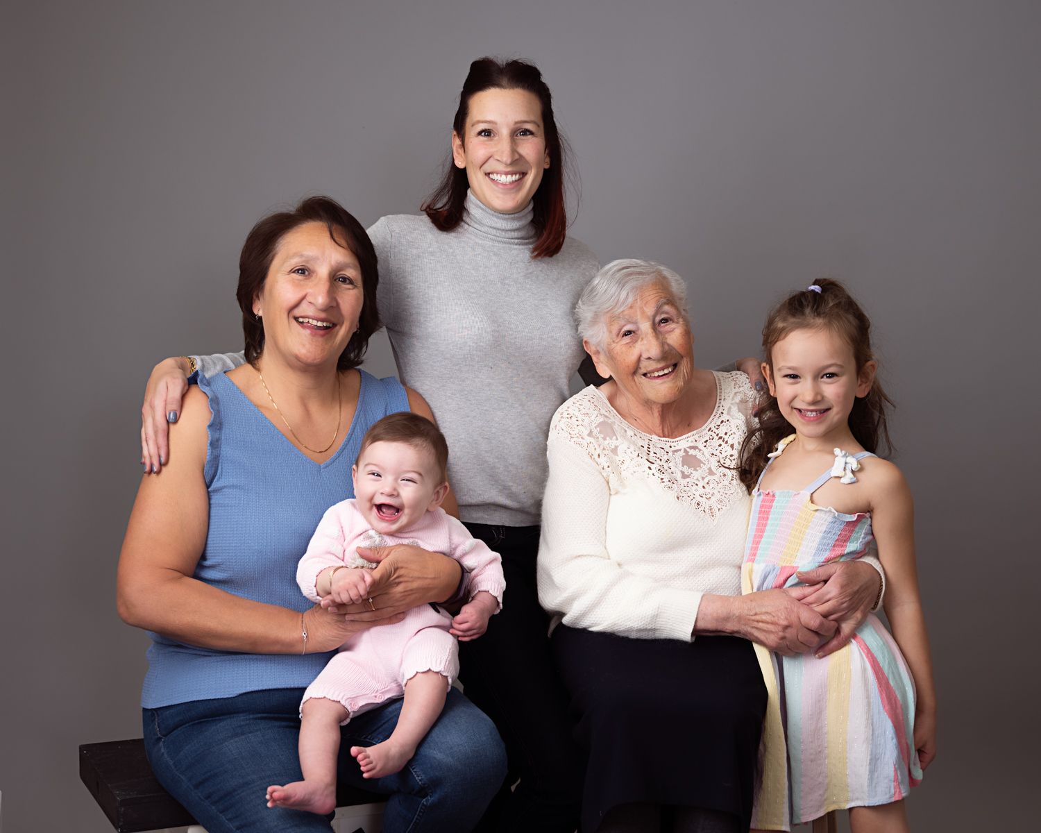 Multi-generational family portrait in studio against gray background.