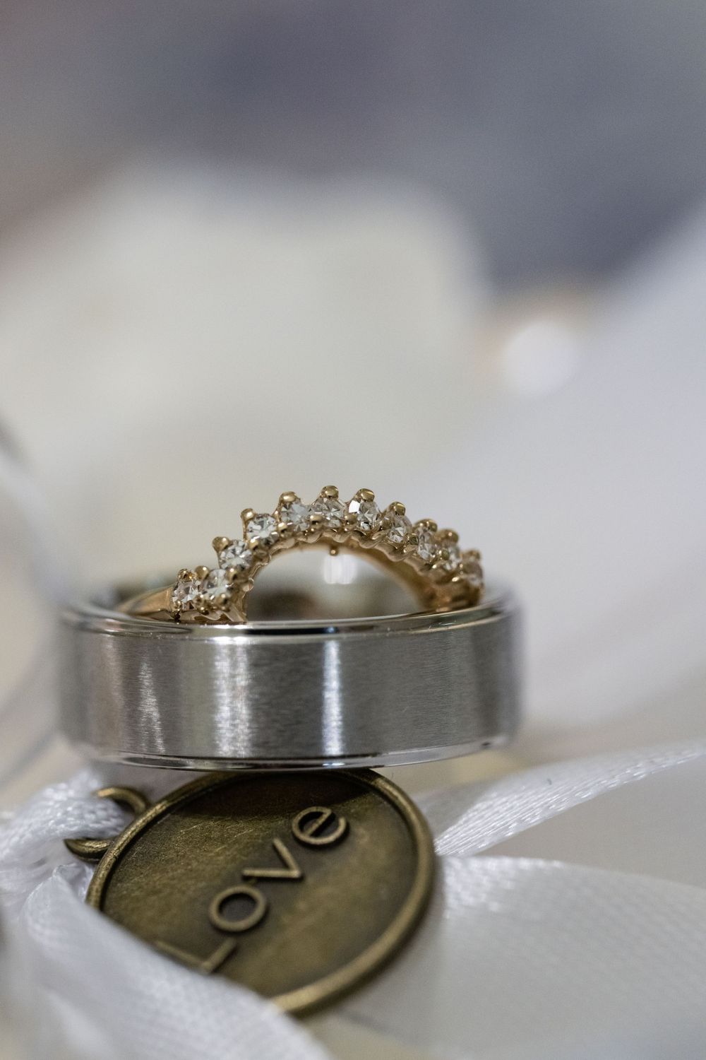 Wedding rings and love charm photographed in macro detail on white fabric.