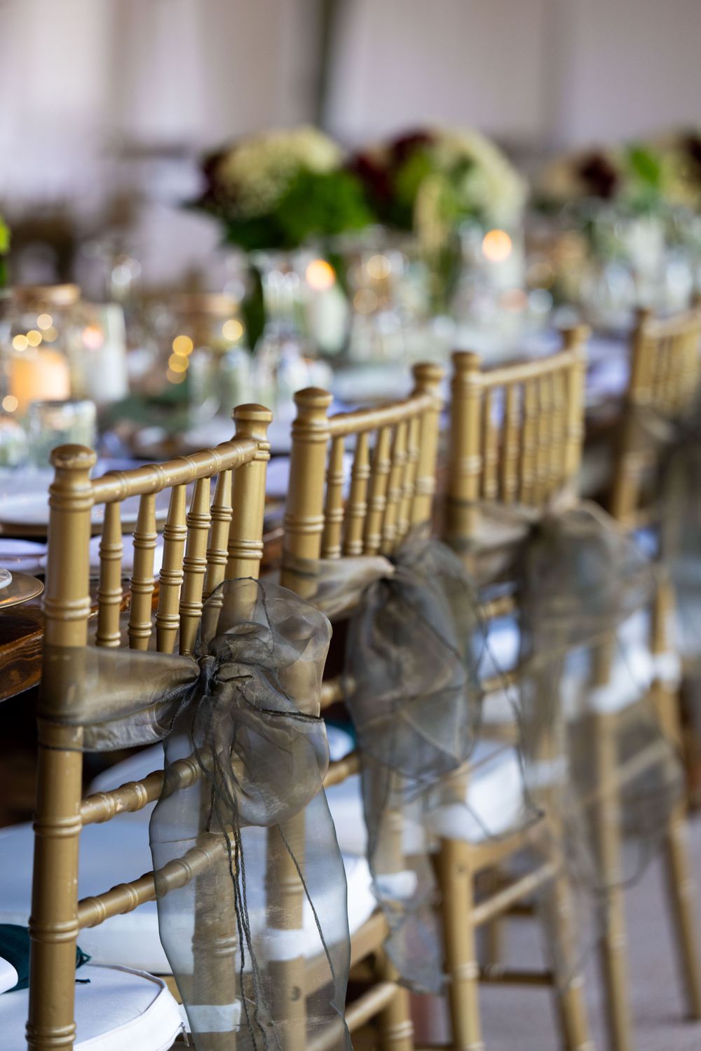 Elegant gold chiavari chairs with gray ribbon bows line wedding reception table.