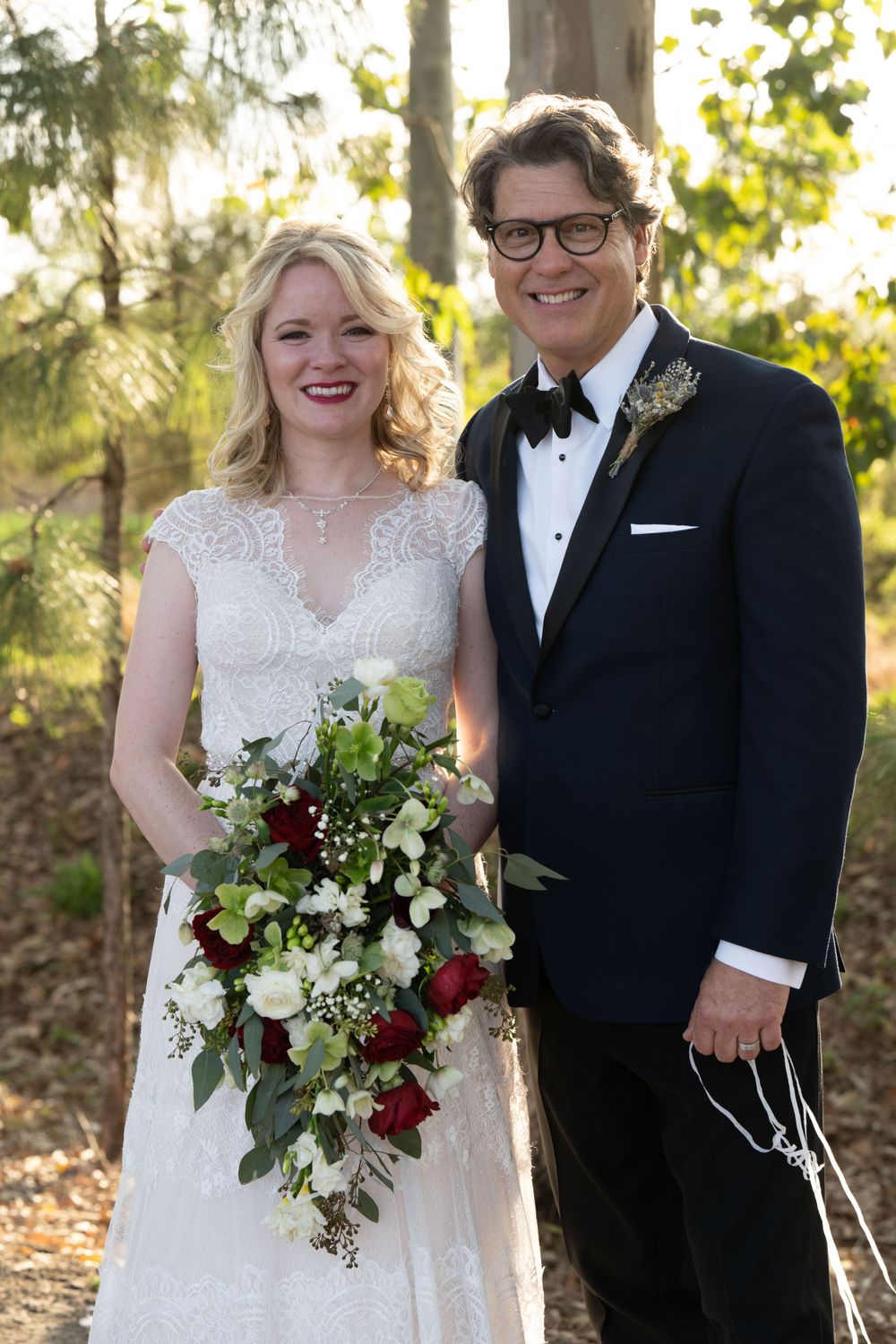 Elegant couple on their wedding day outdoors in formal attire with a lush burgundy and white bouquet.