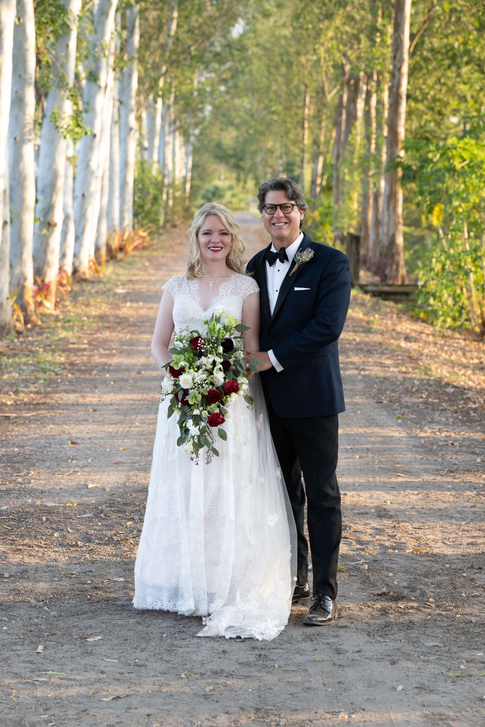 Newlyweds pose together on forest path lined with birch trees during autumn wedding.