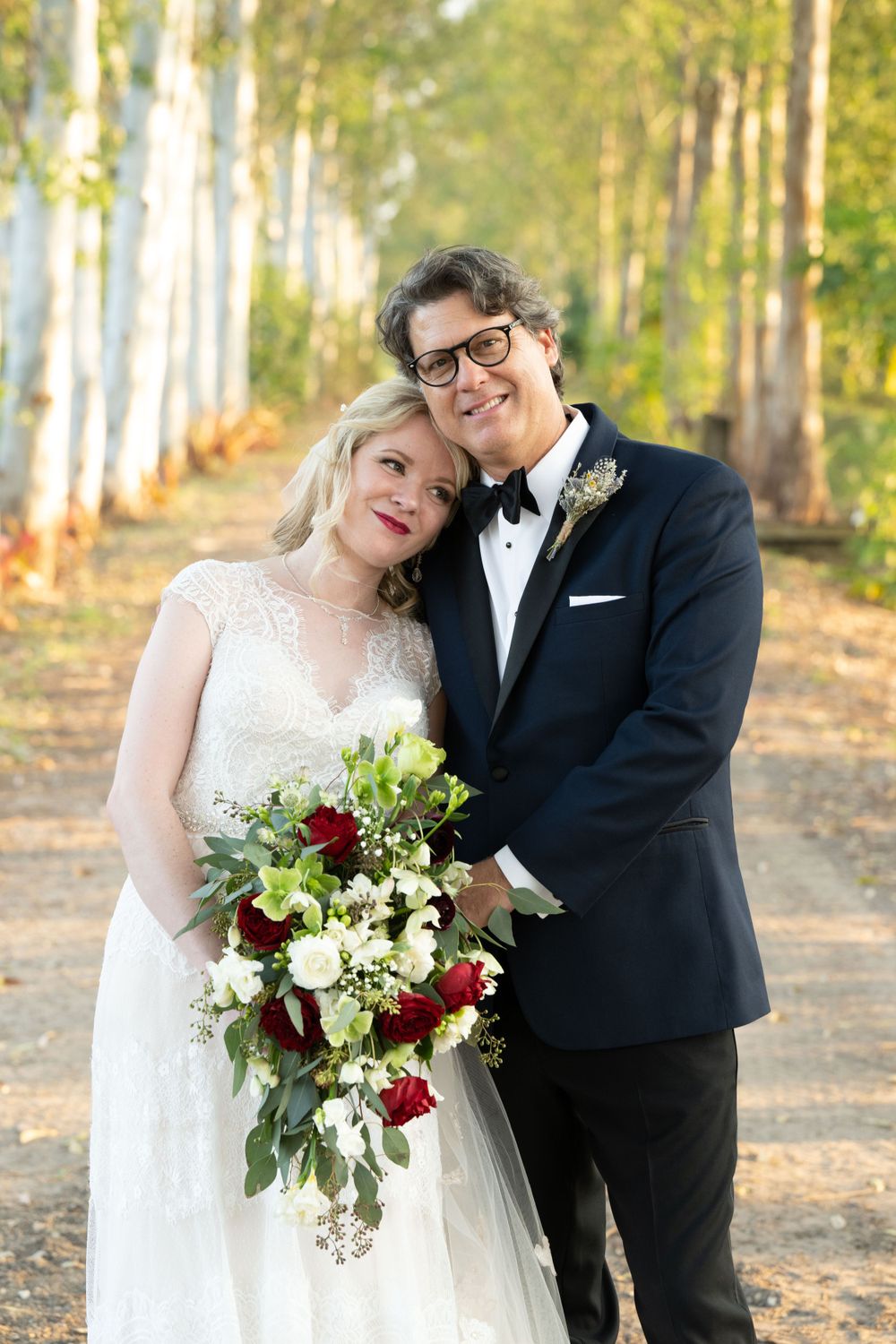 Romantic wedding portrait of couple among birch trees with burgundy and white floral bouquet.