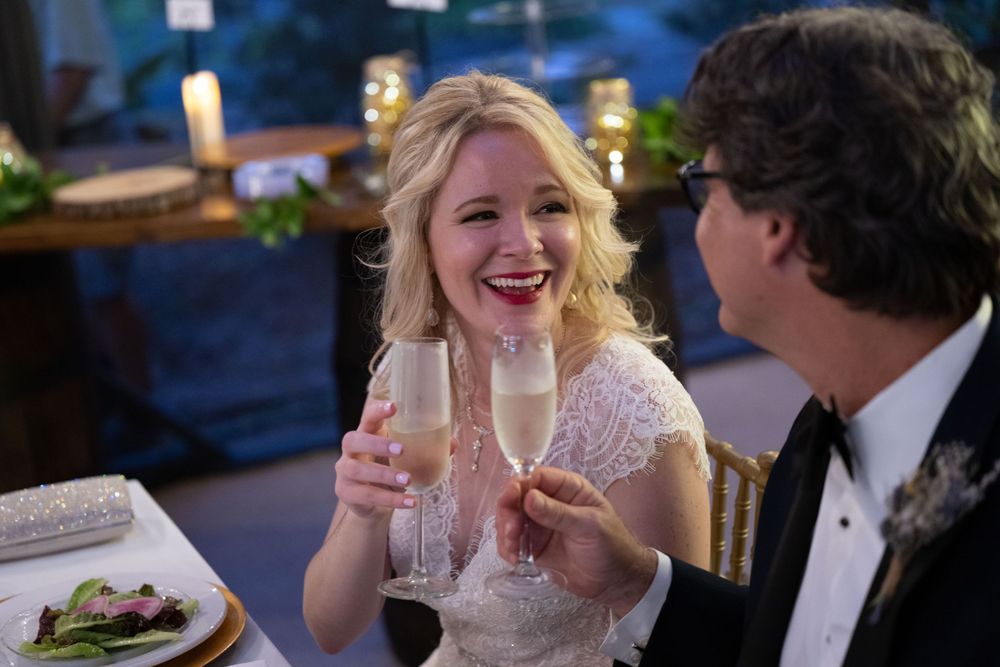Newlyweds share champagne and laughter during evening wedding reception.