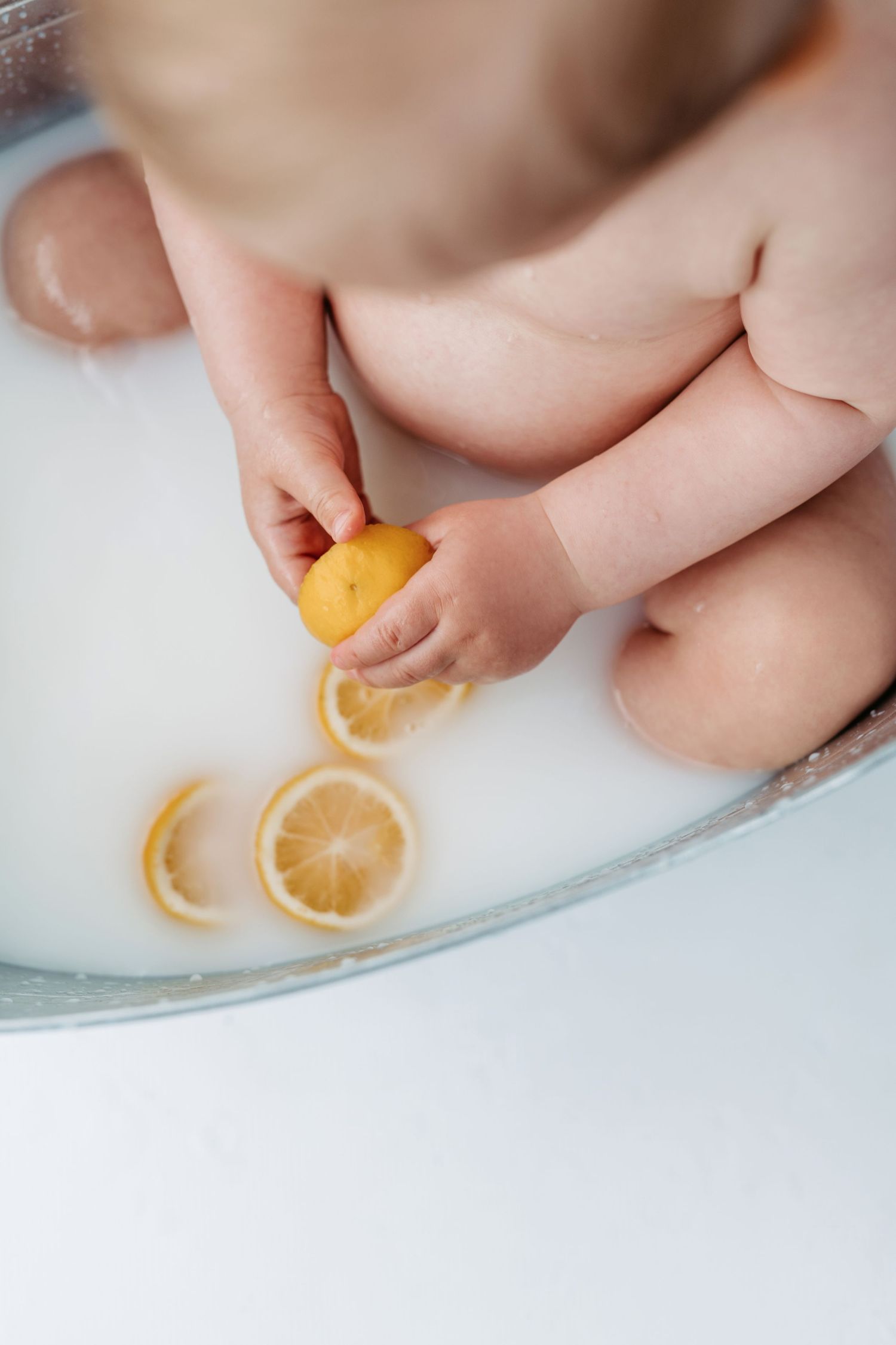 Small hands play with fresh lemon slices in a milky bath.