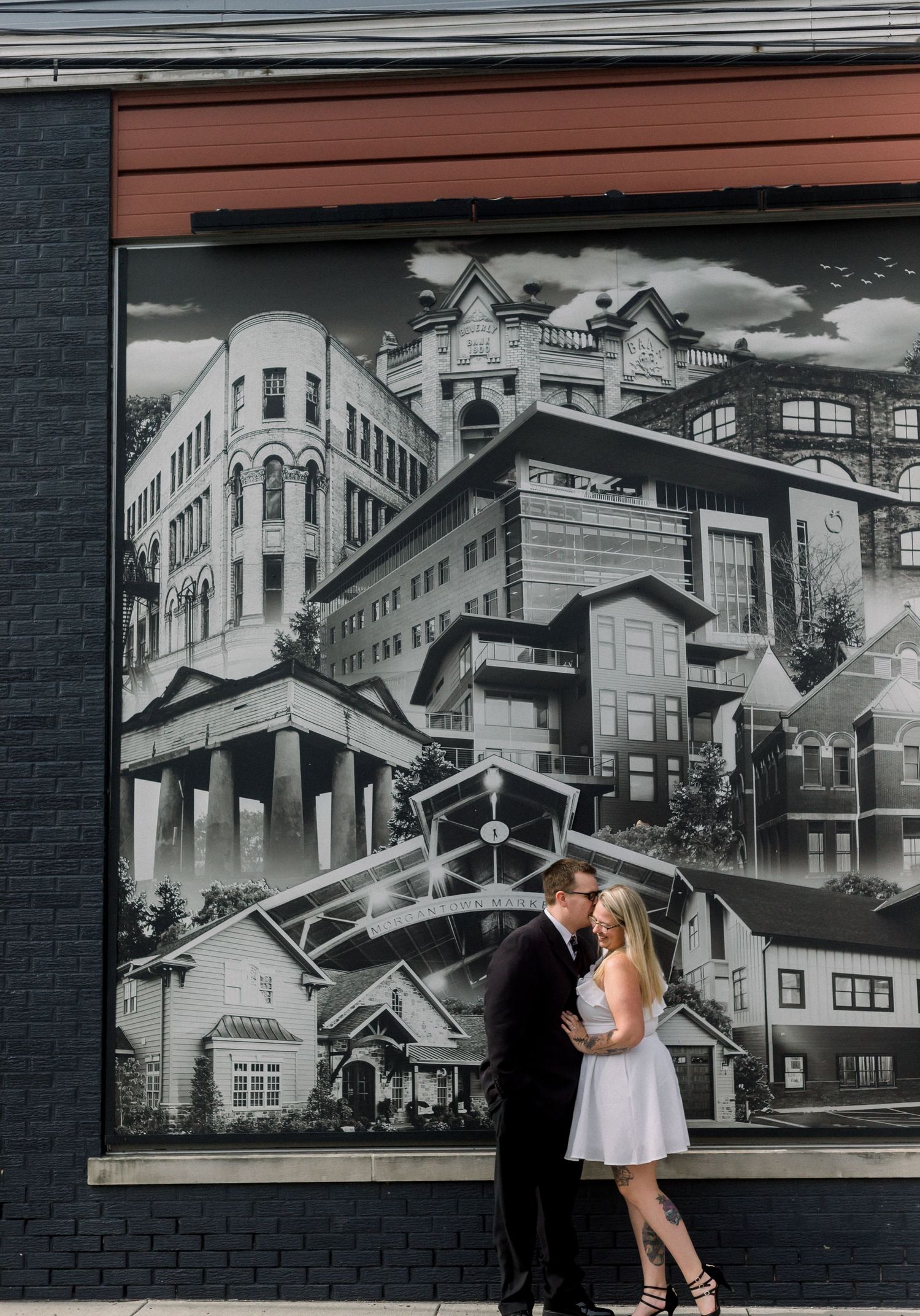 A couple poses against an urban mural featuring black and white cityscapes.