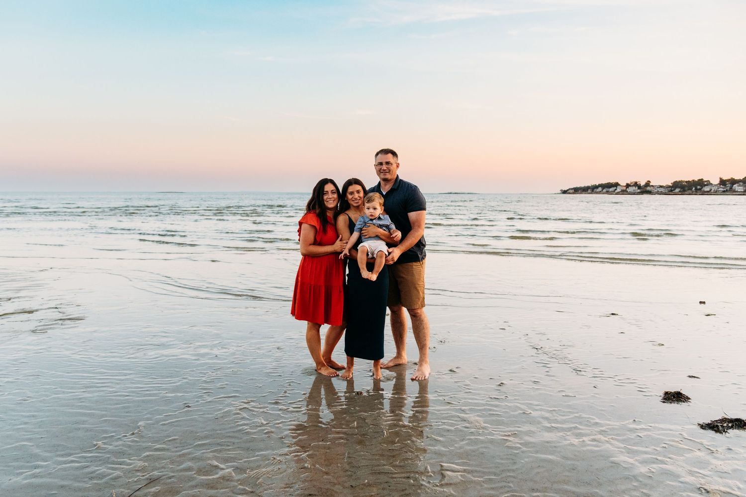 Beachside family portrait at sunset with gentle waves washing shore.