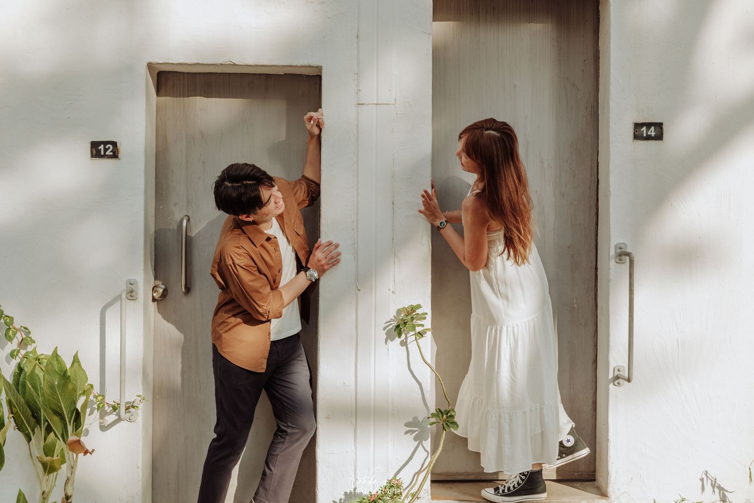 A playful couple interacts near modern elevator doors in a bright hallway.