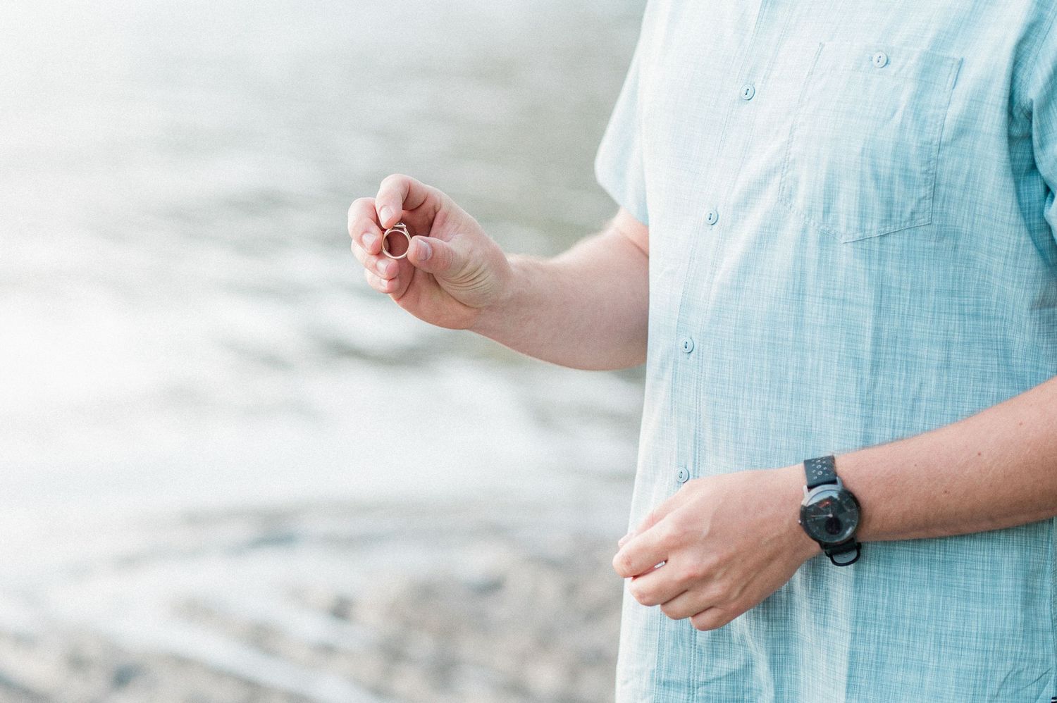 Groom holding up wedding ring with lake in the background