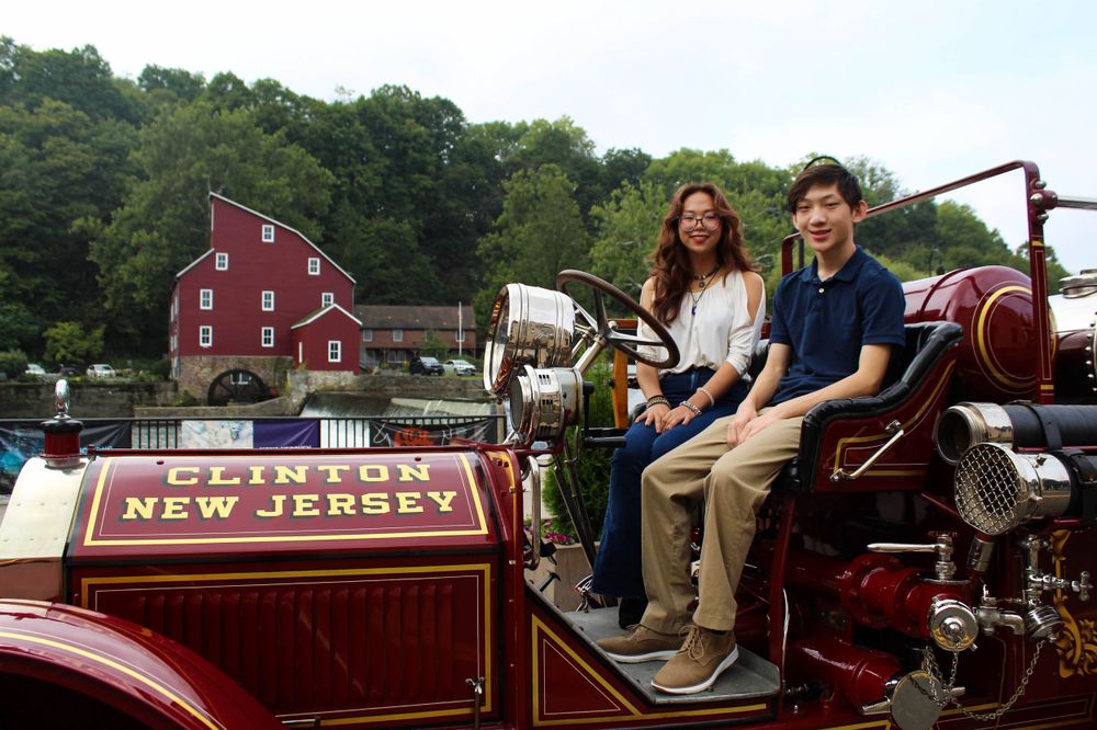 Two people sit on an antique New Jersey fire truck with a red barn in the background.