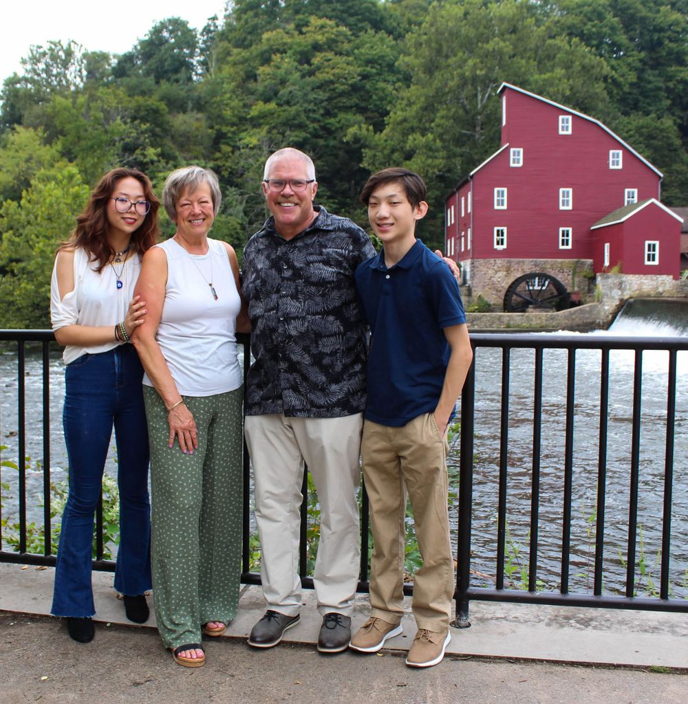 Group photo of four people standing by iron railing with iconic red mill and waterfall behind them.