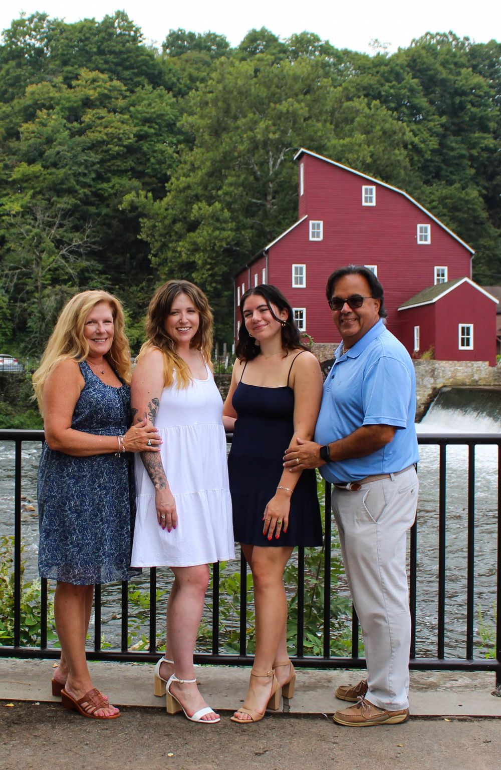 Four people pose on a railing with a scenic red mill and waterway in the background.