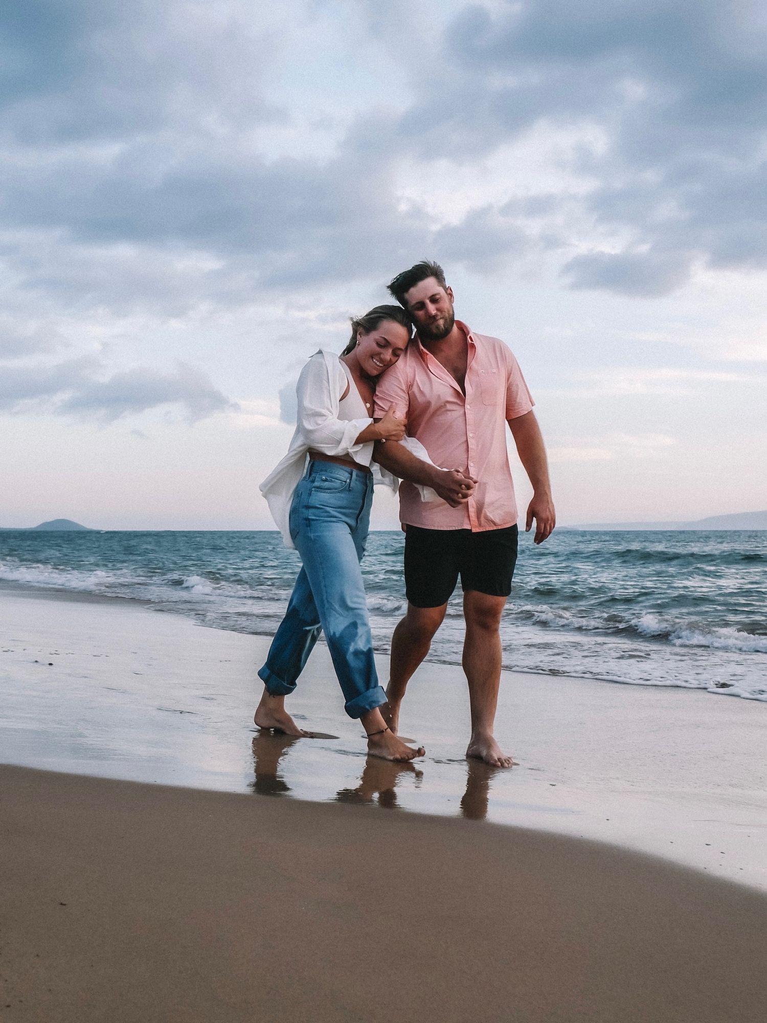 Couple walking and laughing together along the shoreline at dusk.