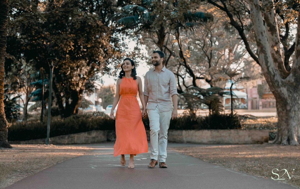 Couple walking together on a tree-lined path, with the person in orange dress and another in grey outfit.