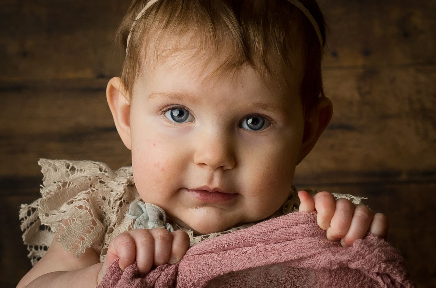 Close up portrait of a baby with rosy cheeks against a rustic wooden background.