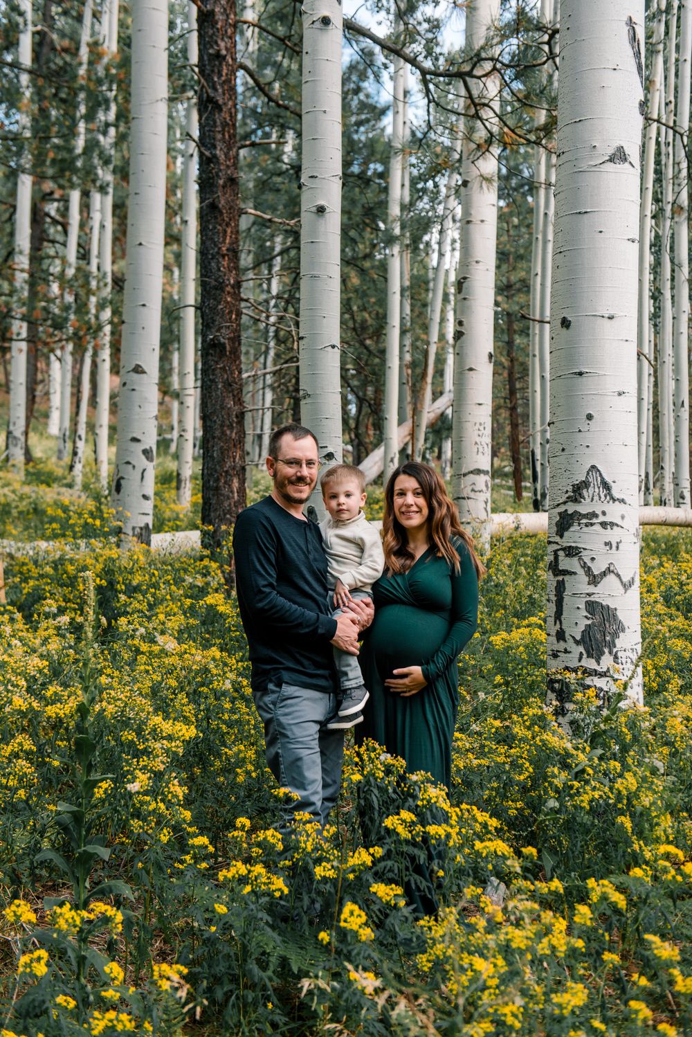 A family stands together in an aspen grove with yellow wildflowers carpeting the forest floor.