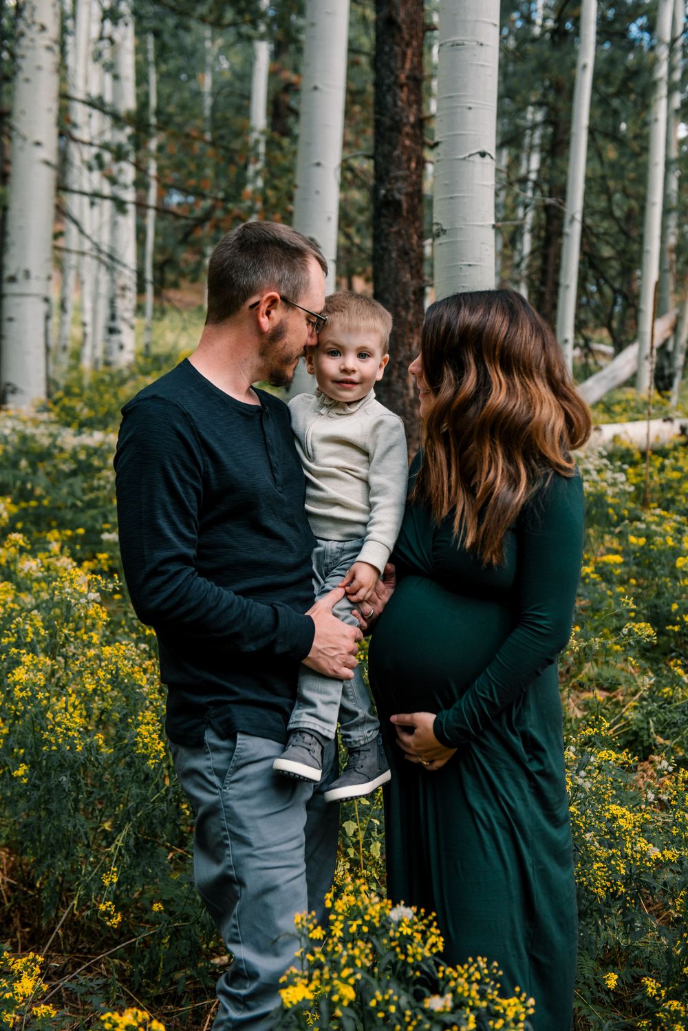 A family shares a tender moment among white aspen trees and yellow wildflowers.