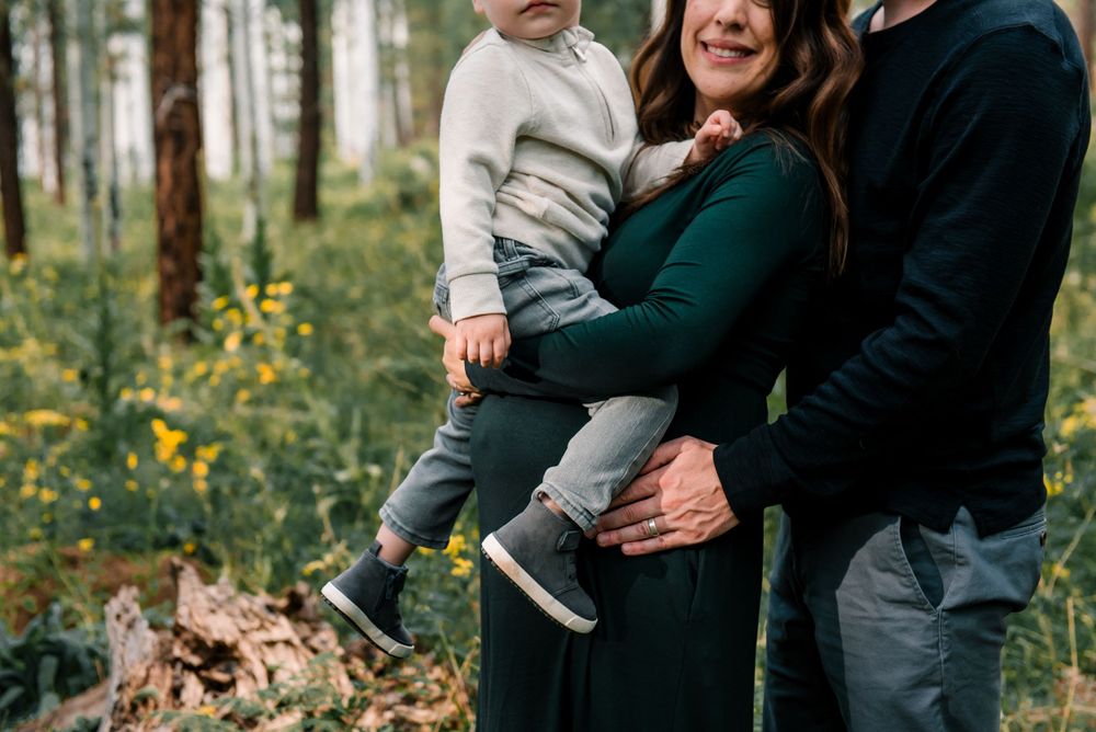 A family shares a joyful moment together in an aspen forest with yellow wildflowers blooming below.