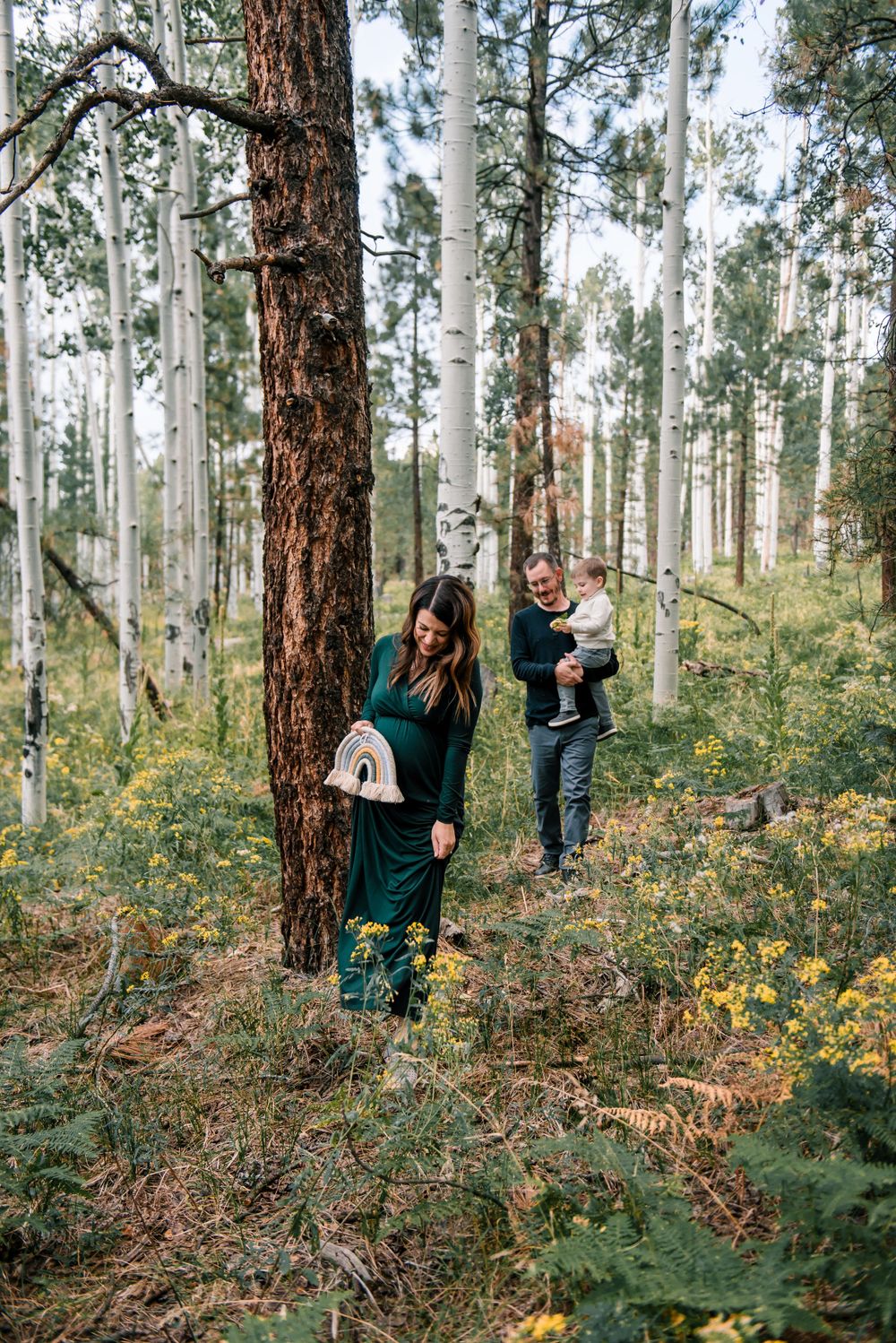 Family members interact playfully among birch trees and yellow wildflowers in a forest.