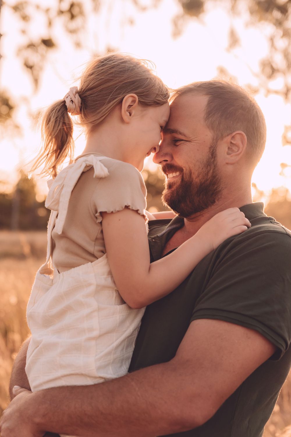 Father and daughter touching foreheads in a field at sunset in Townsville