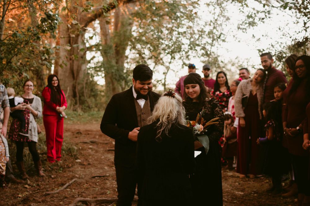 Wedding guests gather around a couple during an outdoor forest ceremony.