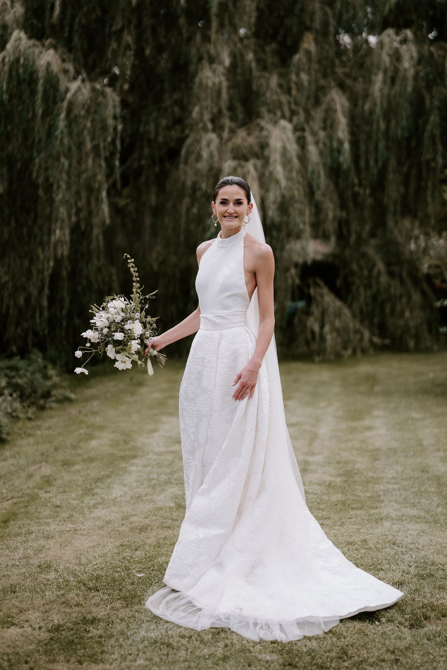 bride stood under willow tree smiling in gardens in islip, oxforshire