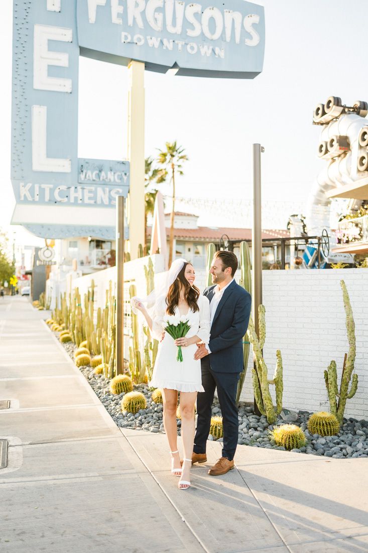 A sunny portrait of a couple standing together outside Ferguson's Downtown with desert landscaping.