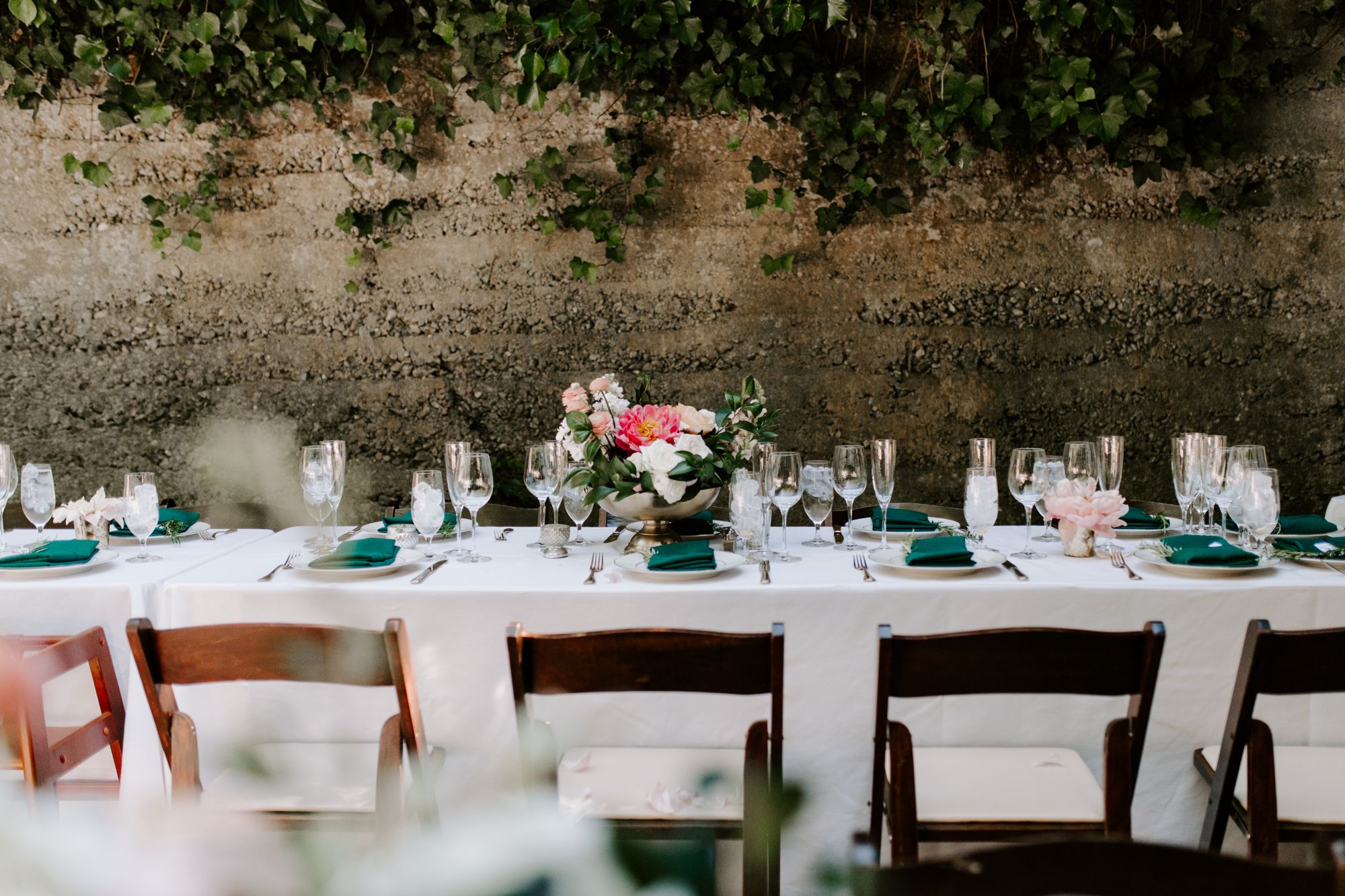 Long banquet tables set with elegant place settings in emerald green and white for a wedding reception.