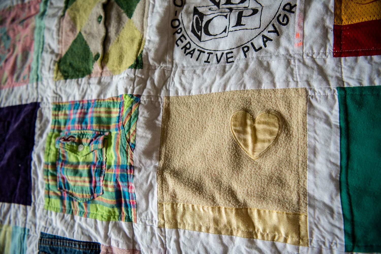 Memory quilt made with baby clothes with a. yellow fleece blanket square with a heart on it.