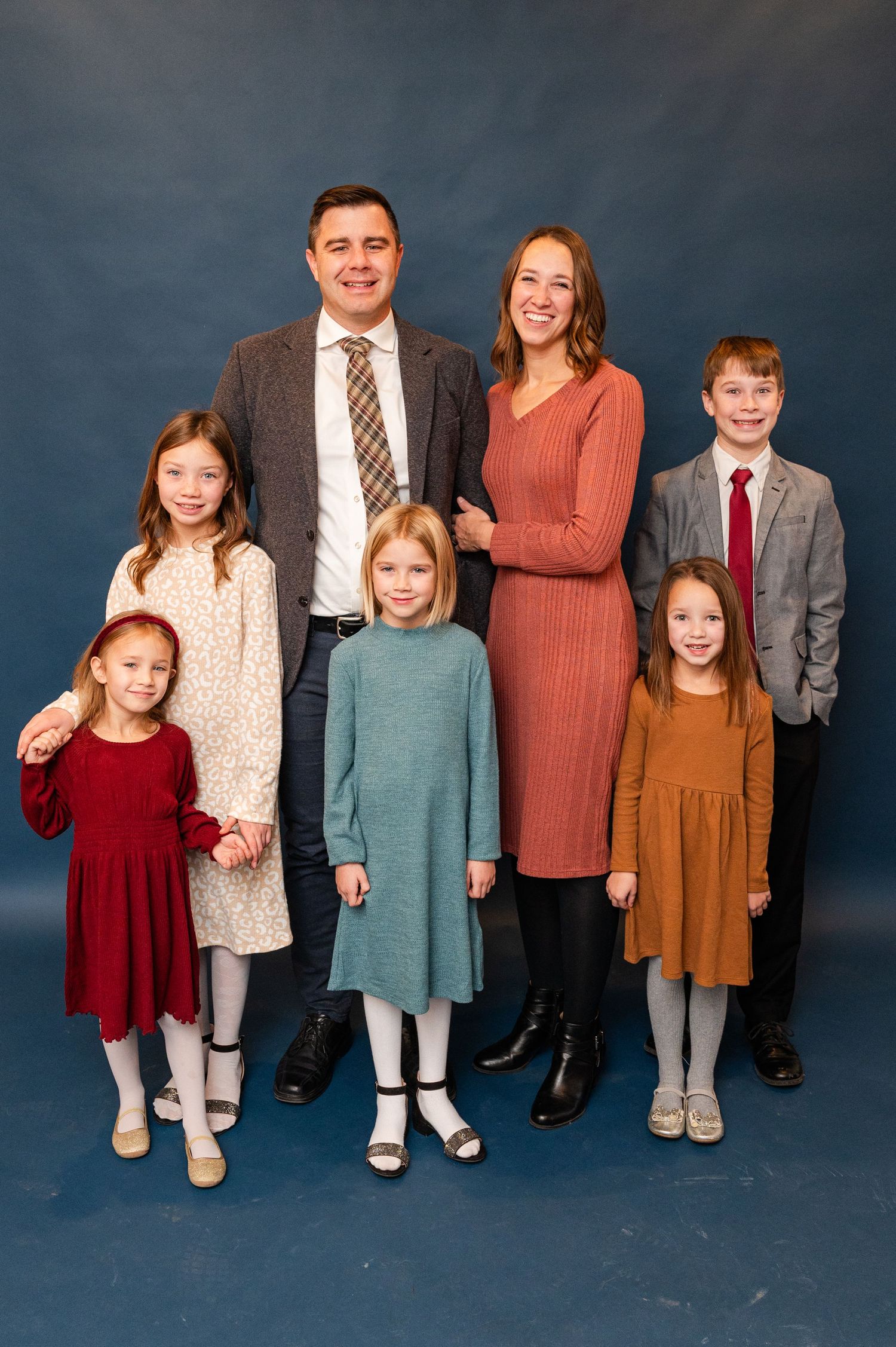 Family portrait of seven people against blue backdrop in coordinated winter outfits.