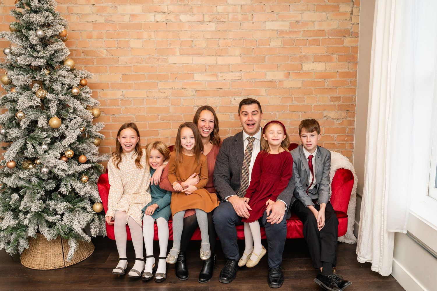 Family holiday portrait with decorated Christmas tree against brick wall.