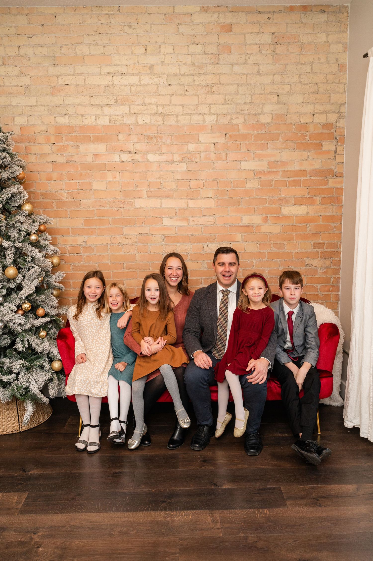 Family of seven seated on red couch for Christmas portrait with decorated tree.