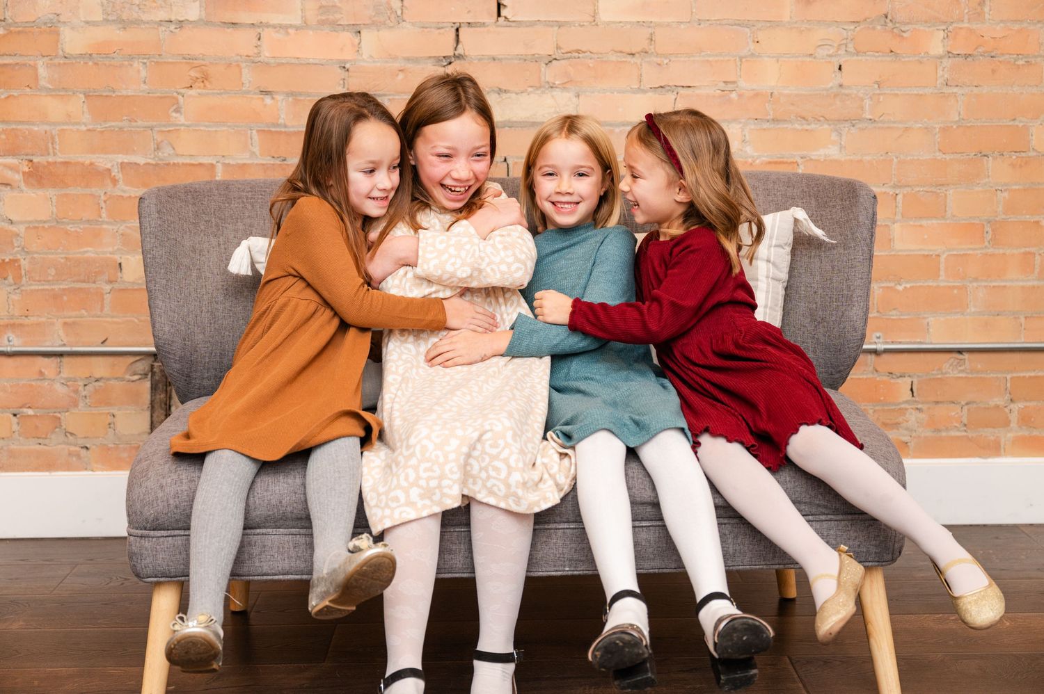 Four young girls in colorful dresses sitting together on grey bench.