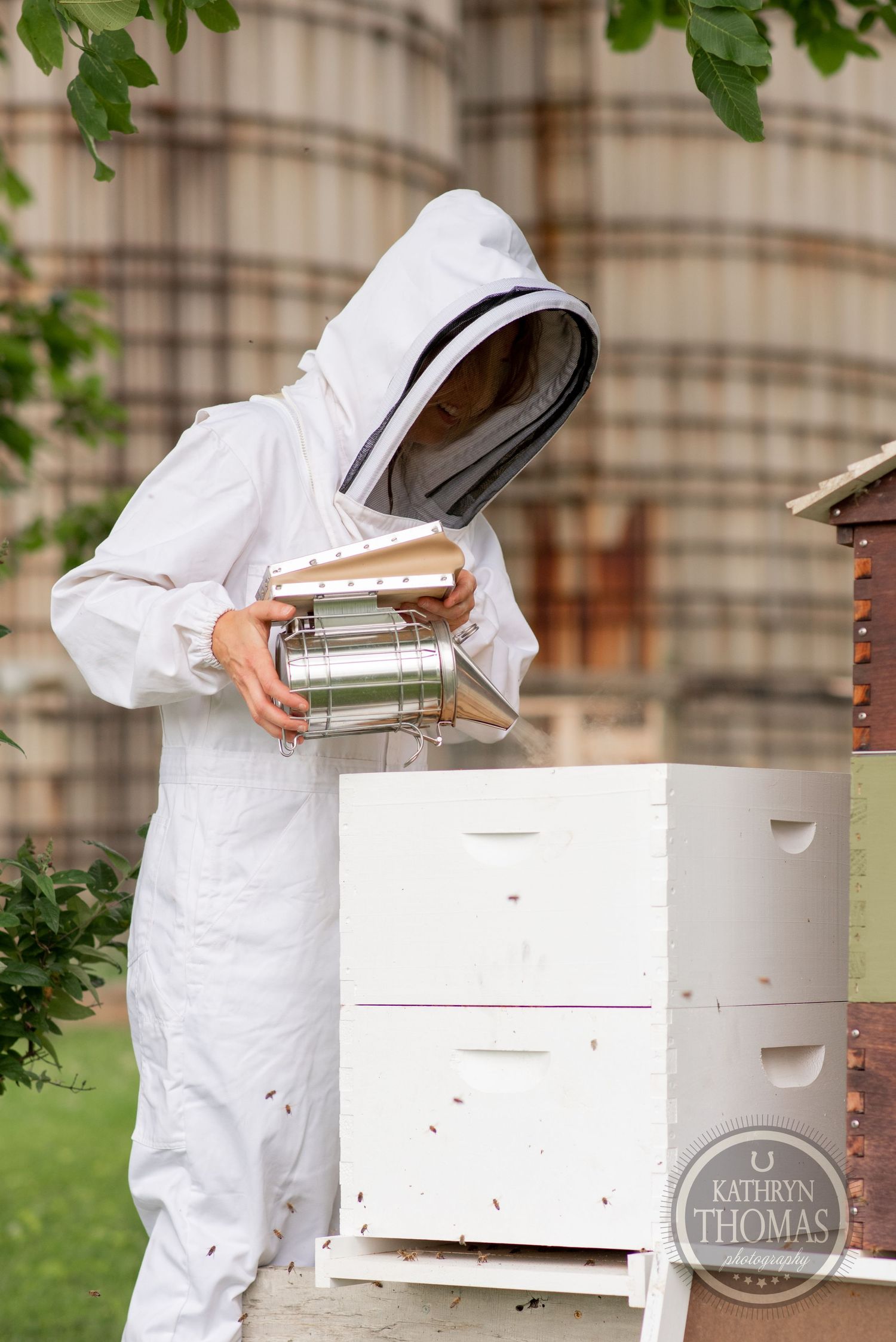 Beekeeper in white protective suit handling equipment near stacked white hive boxes.