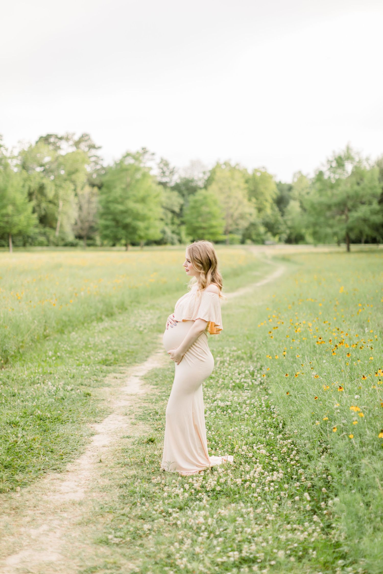 A serene maternity photo in a meadow with yellow wildflowers and a natural pathway.