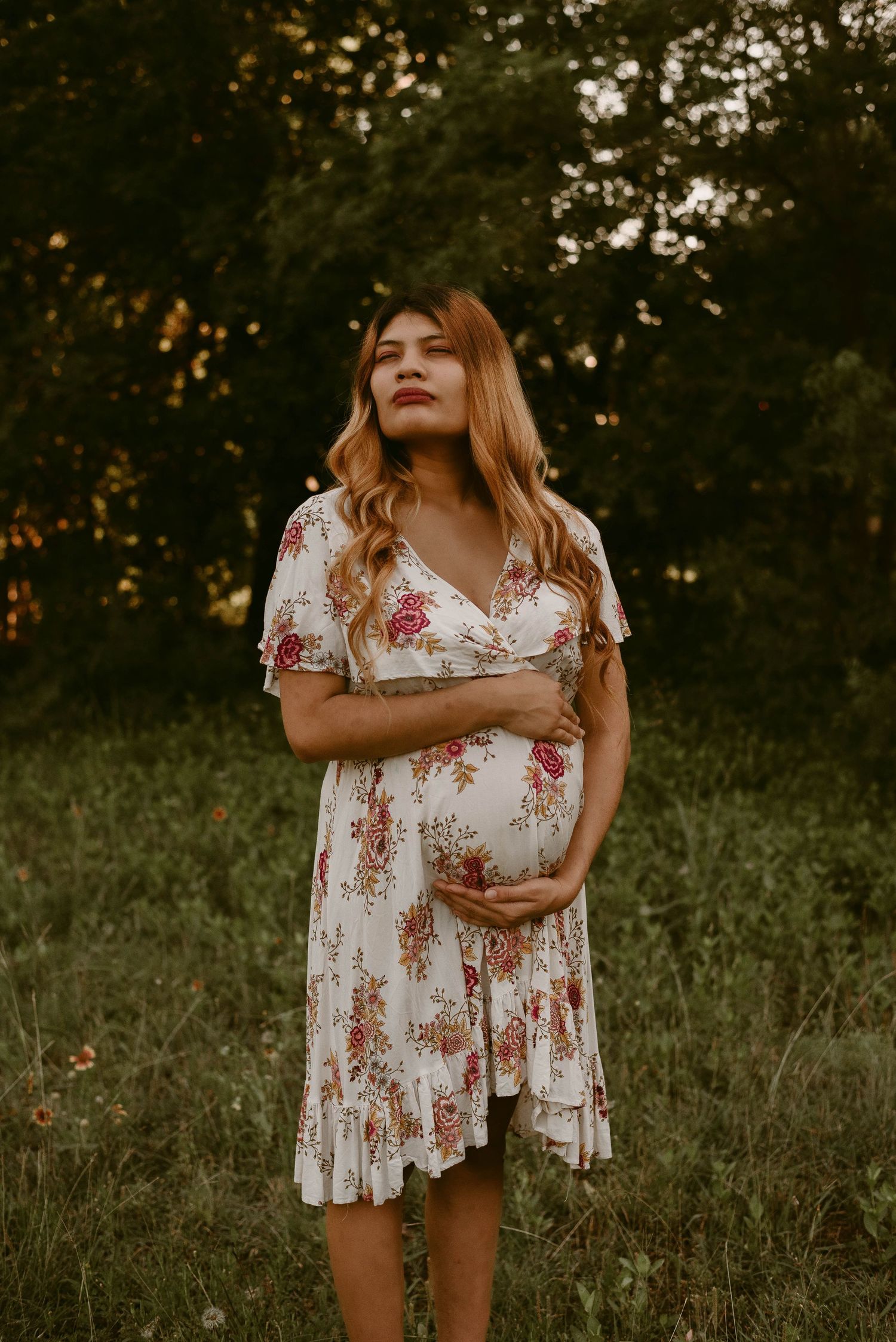 Sunset maternity photo featuring flowing white floral dress in outdoor garden setting.