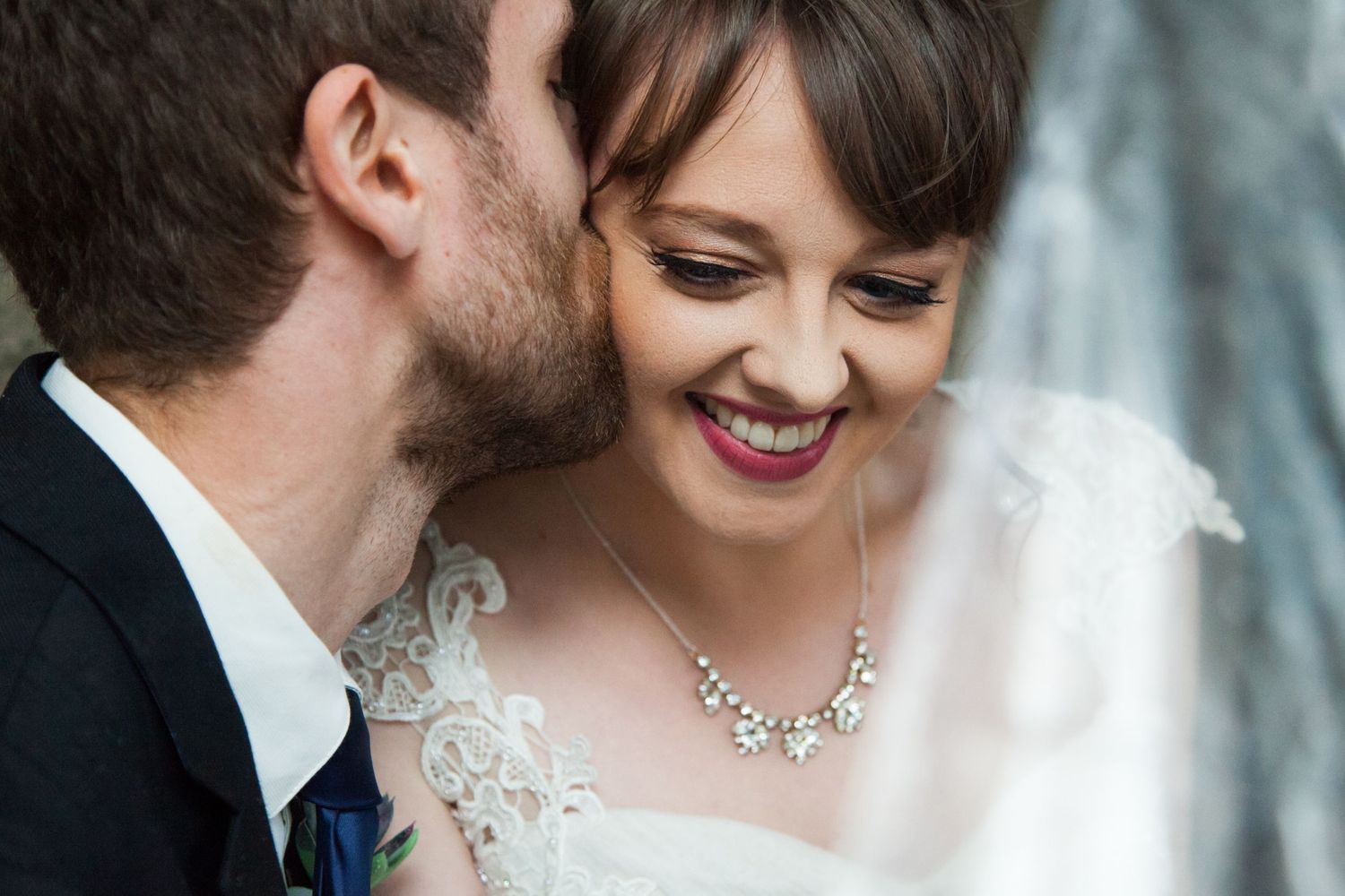 Close-up of couple sharing intimate moment showing bride's lace dress and necklace.
