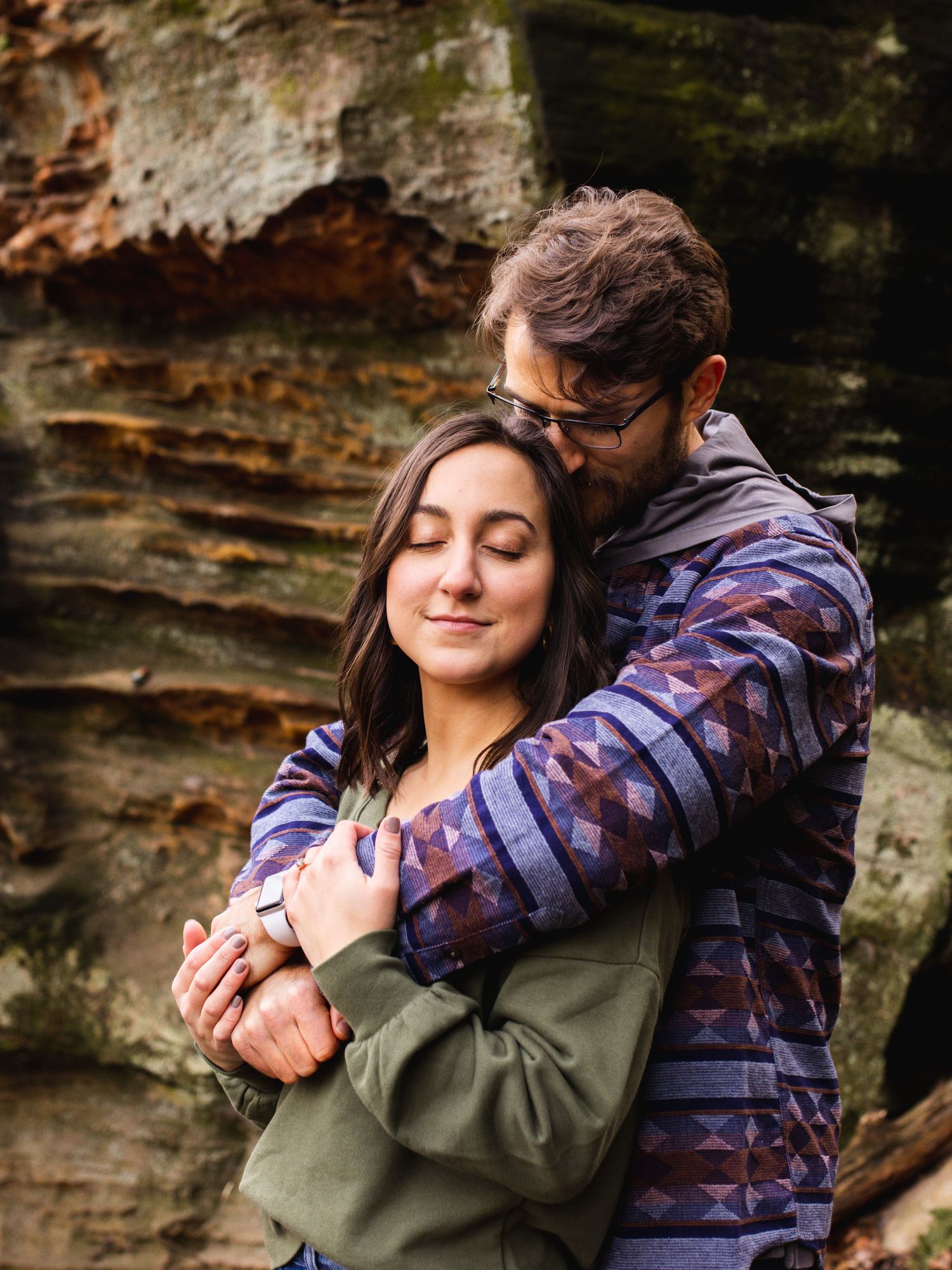 couple by rock formation embracing with eyes closed