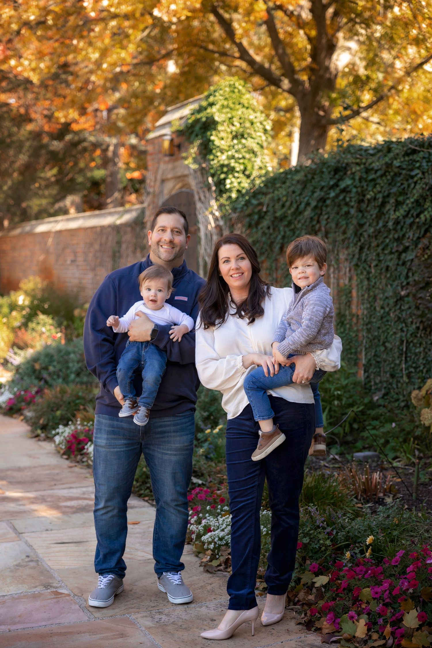 Family of four poses on stone path with vibrant fall foliage and landscaping in background.