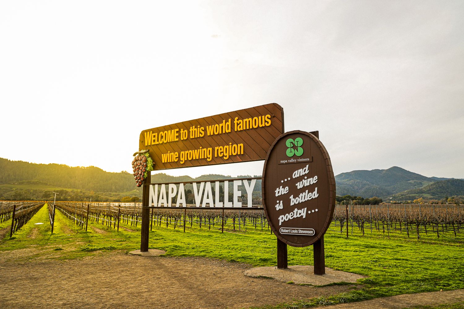 Welcome sign to Napa Valley wine region with vineyard rows and rolling hills during sunset in California.