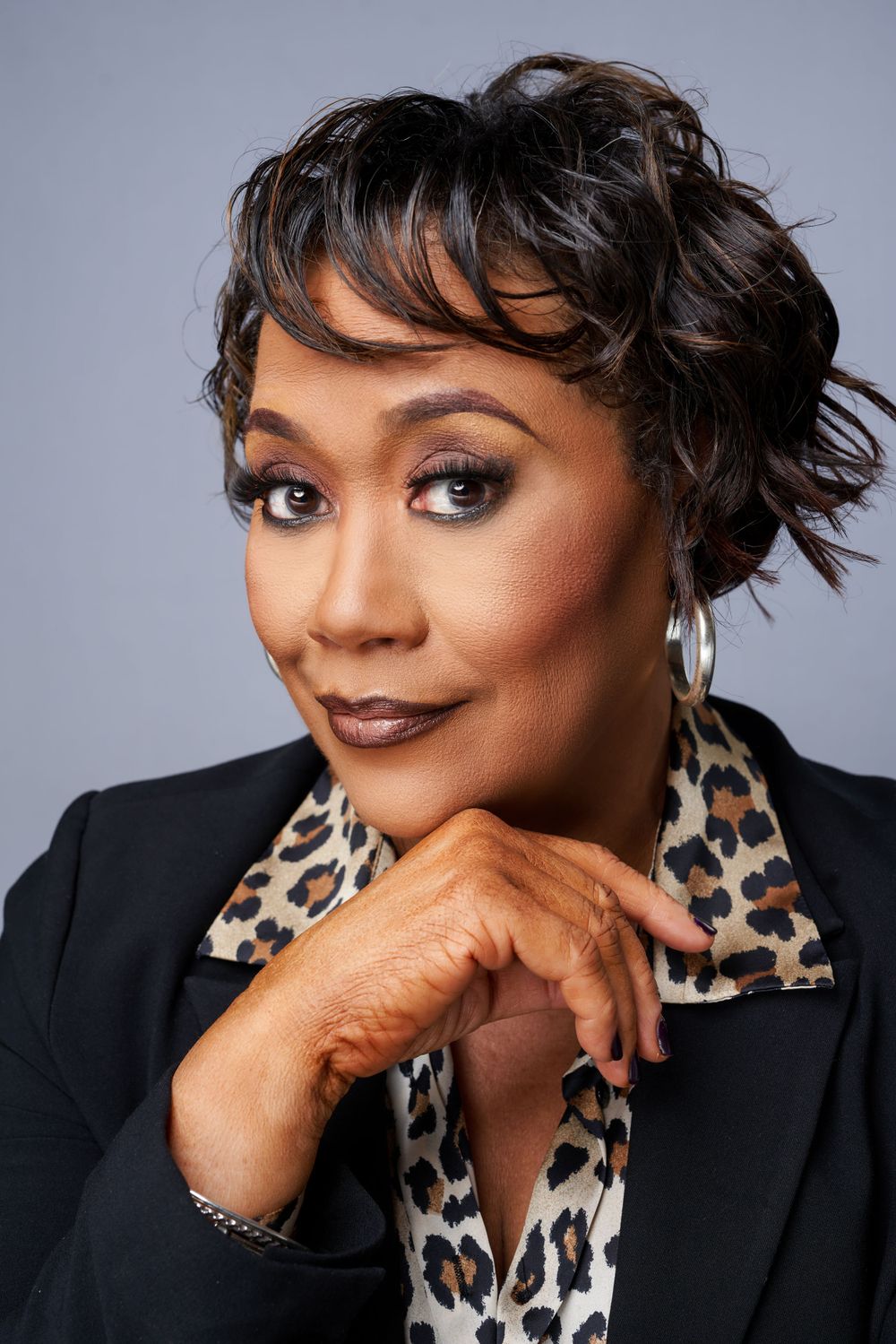 Professional headshot wearing black blazer and animal print scarf against grey background.