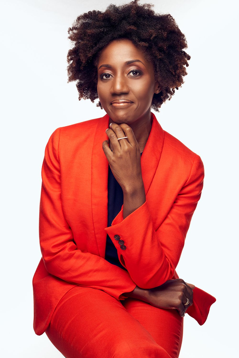 Professional studio portrait in bright red blazer with natural curly hair against white background.