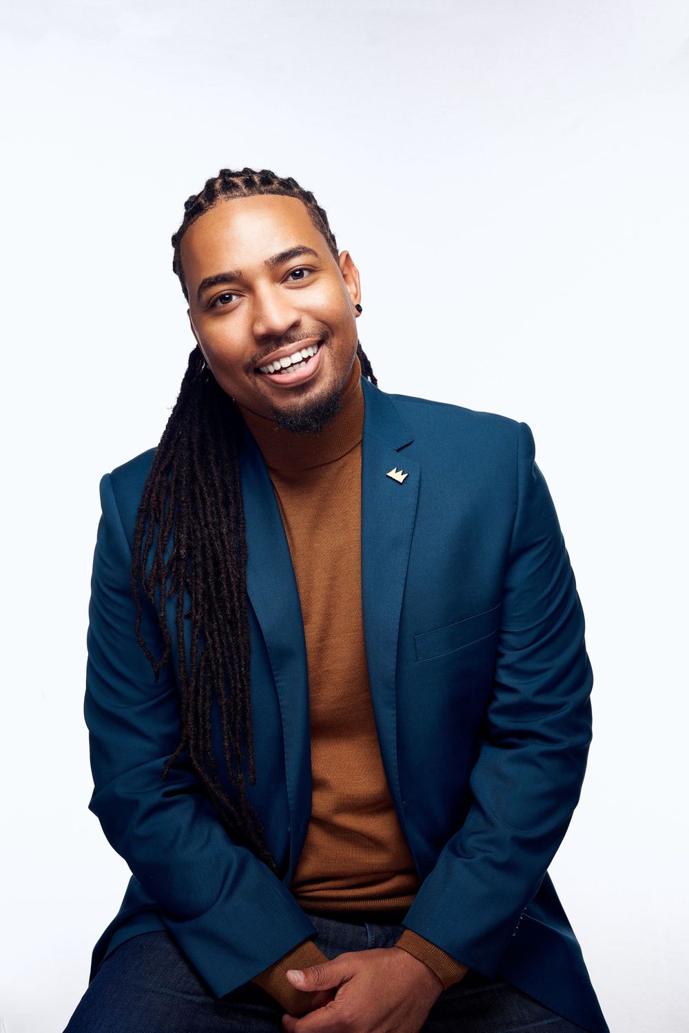 Studio portrait showing person in navy blazer and brown sweater with long braided hair style.